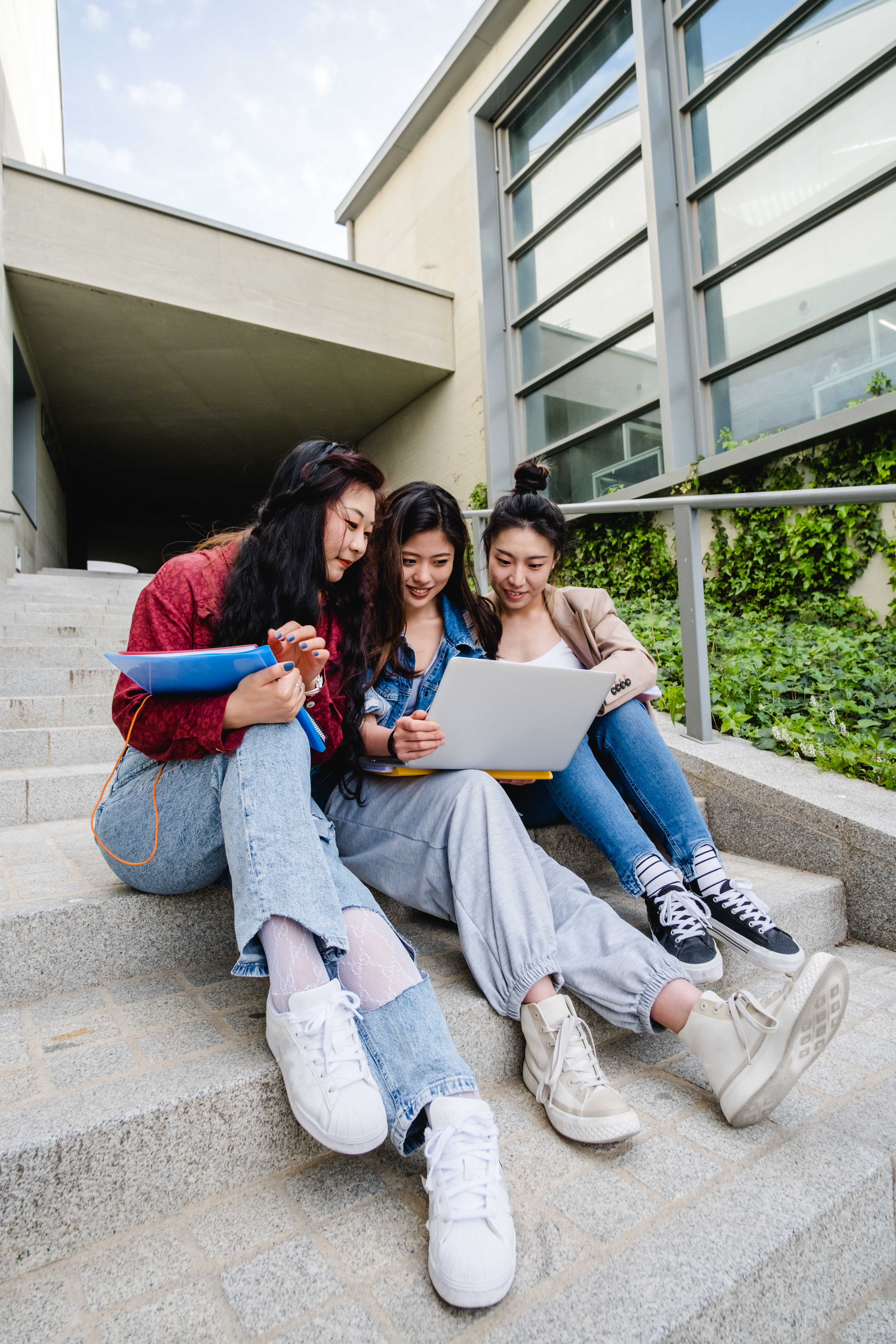 Group of Asian female students using a laptop and studying together while sitting on the stairs of